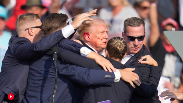 Former president Donald Trump, with blood on his ear, is whisked away from a campaign stage Saturday night following an apparent assassition attempt. AP photo.